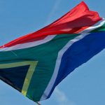 A Fan waves a South African flag as Team Sky rider Froome of Britain, the race leader’s yellow jersey, stands on the podium after the 10th stage of the Tour de France cycling race