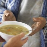 Woman giving bowl of soup to man